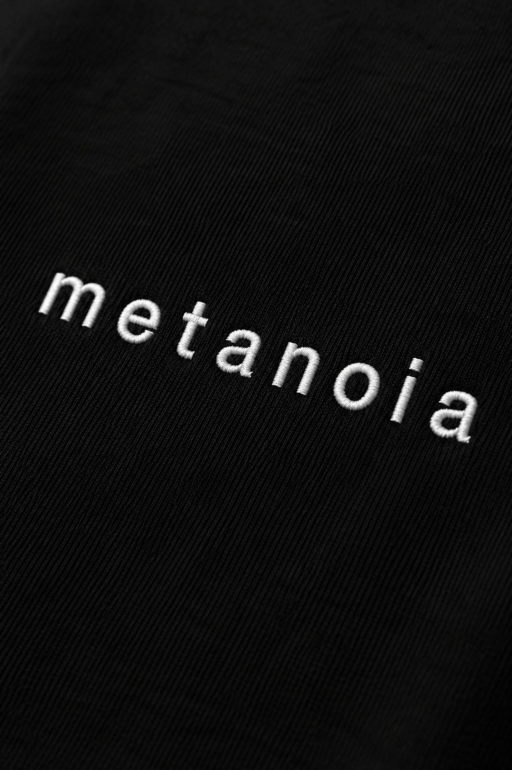 METANOIA embroidered logo detail on black tee