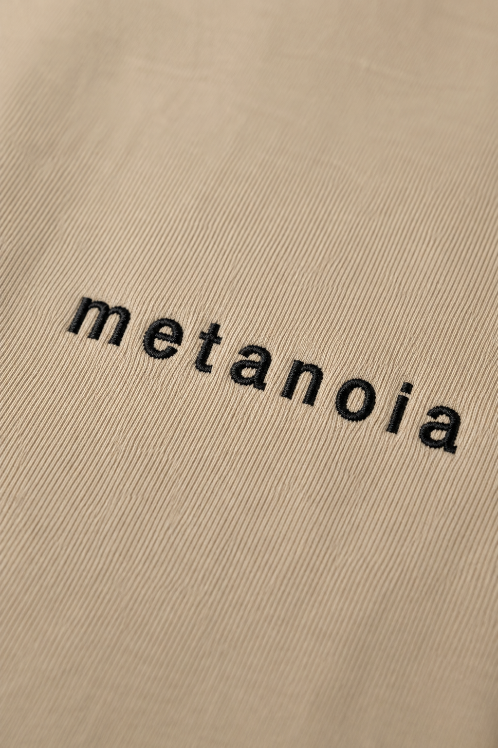 METANOIA embroidered logo detail on beige tee